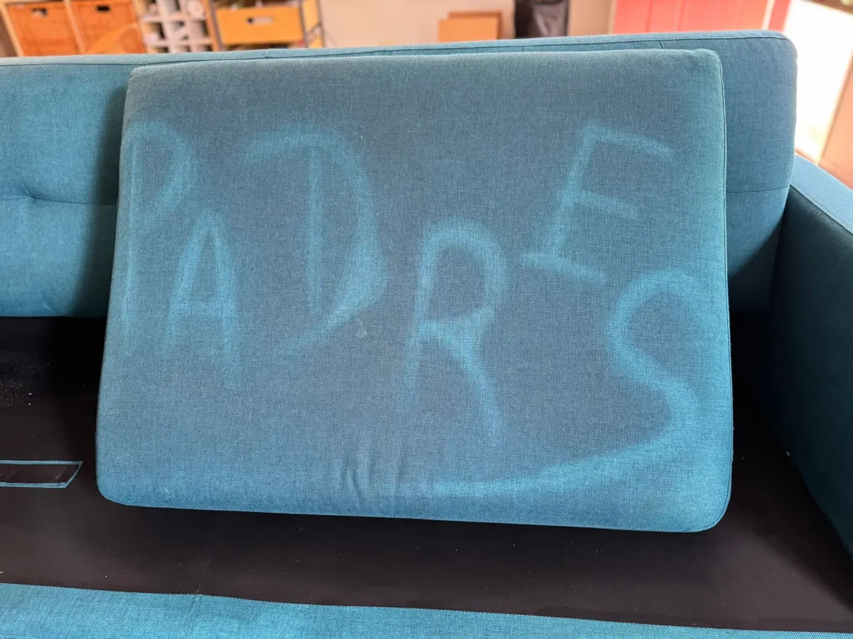 “PADRES” written on a sofa cushion by cleaning, showing hidden soil
